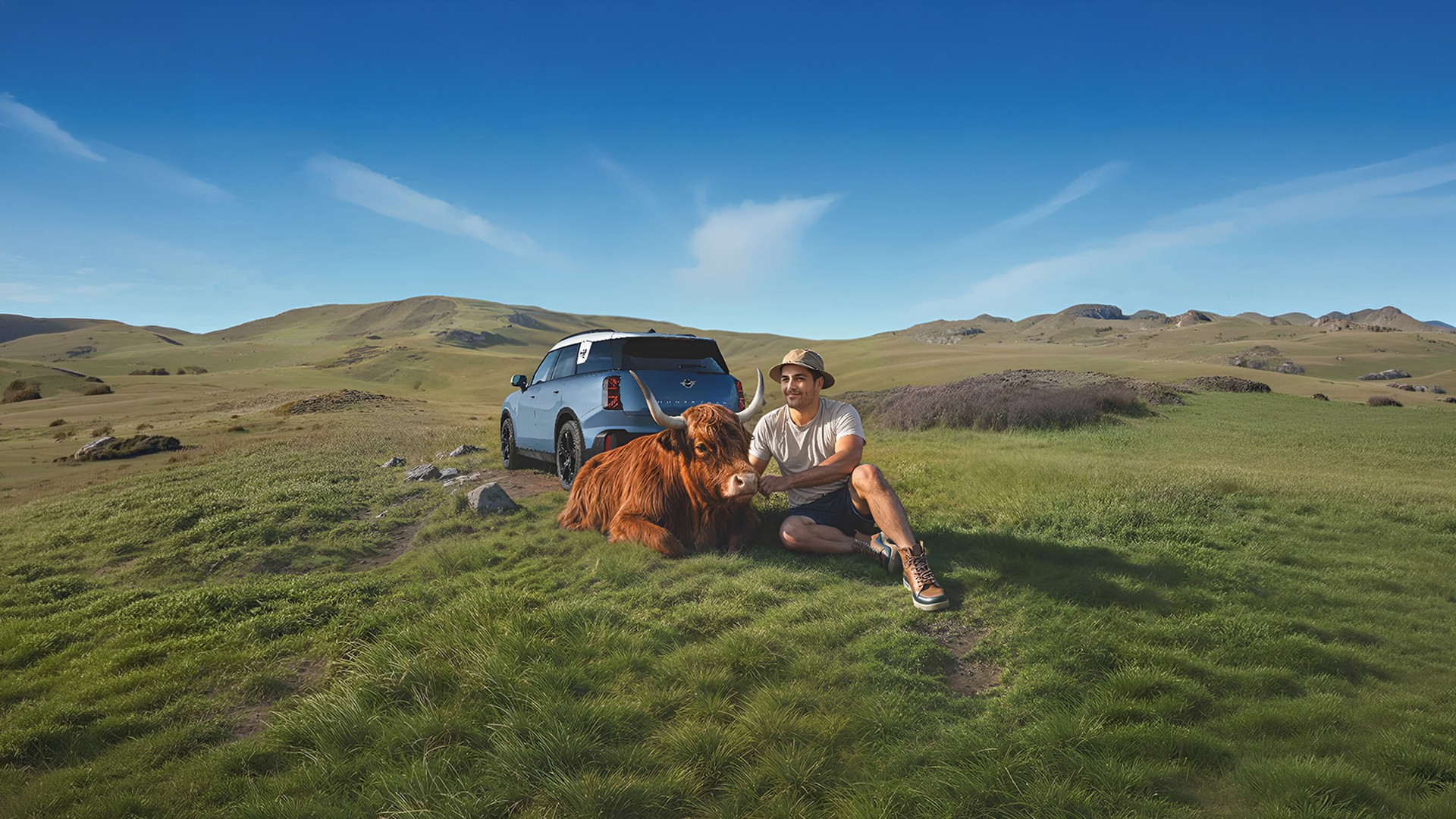 Man outside his MINI Countryman S talking to MINI Roadside Assistance via the MINI App with a  Highland Bull lying nearby.